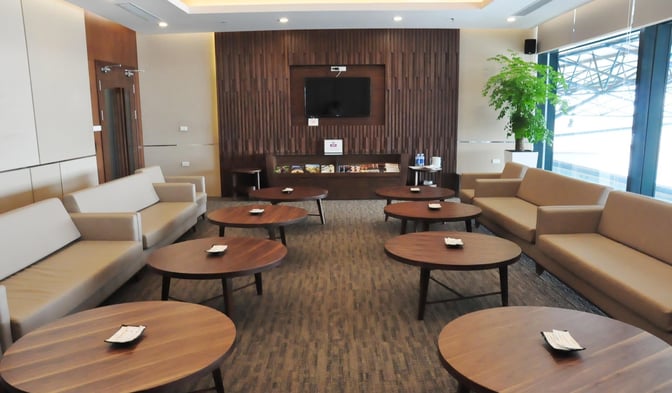 Seating area in Vietnam Airlines Lotus Lounge at Noi Bai Airport features sofas and round tables with a view of the tarmac.