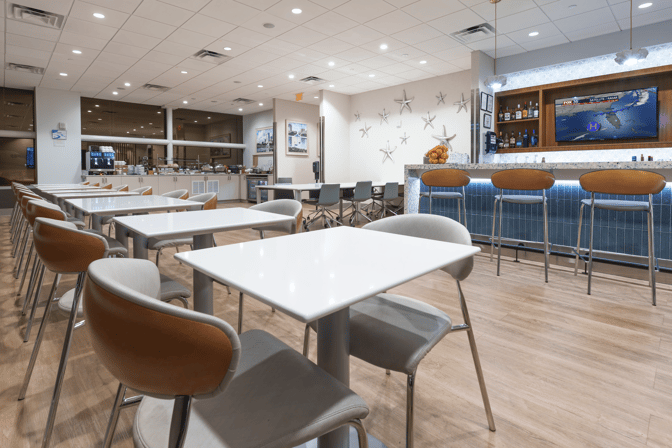 The Club MCO Airside 1 lounge features a bar area with seating and a self-serve food station for travelers.