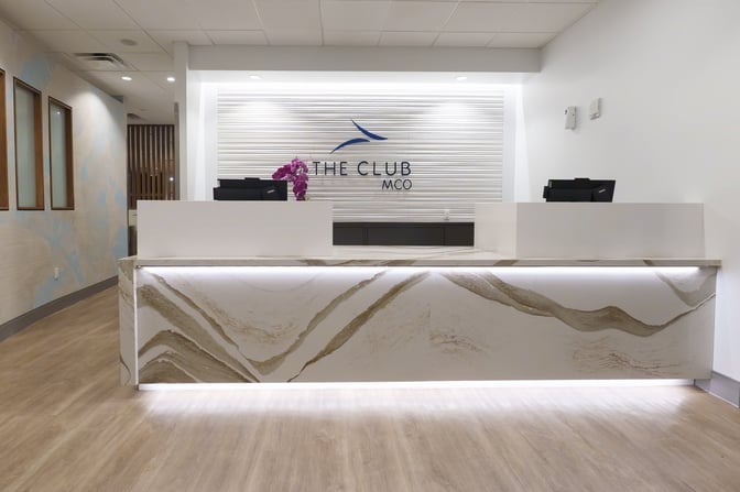 The reception area of The Club MCO at Orlando International Airport features a check-in counter with digital screens and decorative elements.