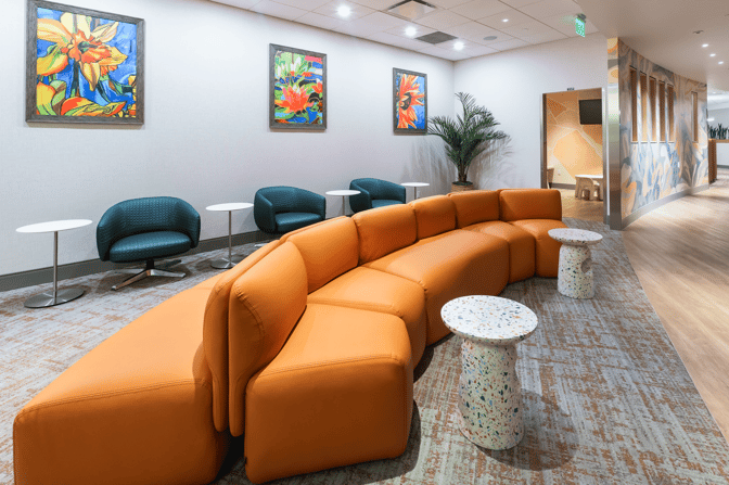The seating area in The Club MCO Airside 4 features curved lounge chairs, small tables, and vibrant artwork on the walls.