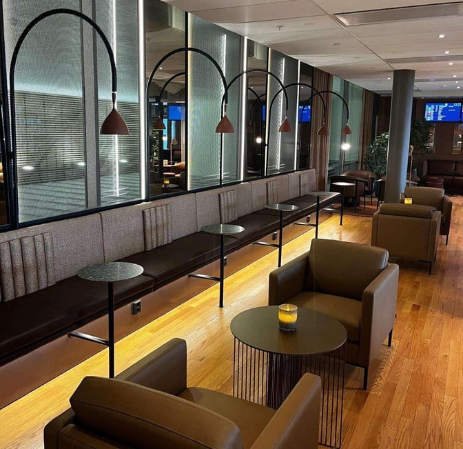 The seating area in OSL Lounge International at Oslo Airport features cushioned benches and armchairs with small tables for travelers.