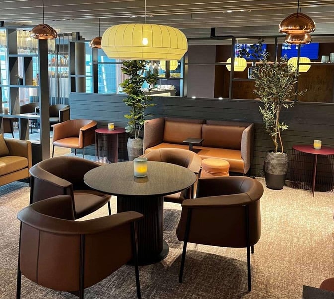 The seating area at OSL Lounge International features round tables with chairs and booth seating, providing a comfortable space for travelers.
