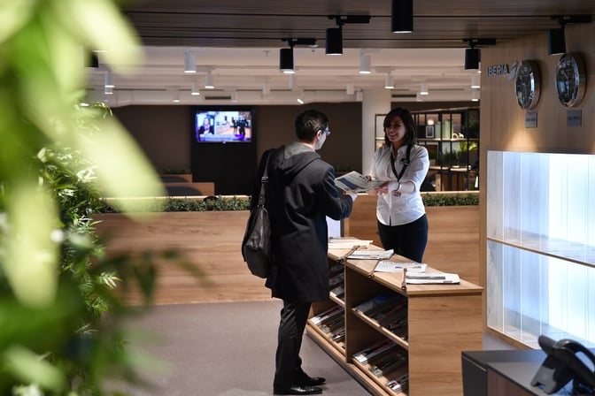 A staff member at the Premium Traveller Lounge in Paris-Orly Airport assists a guest at the reception area with newspapers available.