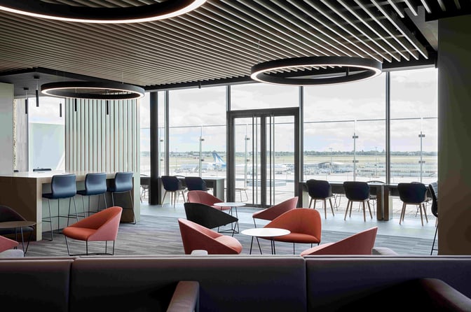 The Primeclass Lounge at Paris-Orly Airport features seating areas with tables and chairs, offering views of the airport runway.