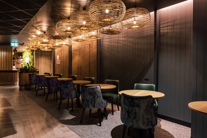 Seating area in the International Aspire Lounge at Perth Airport features round tables and chairs, with decorative overhead lighting.