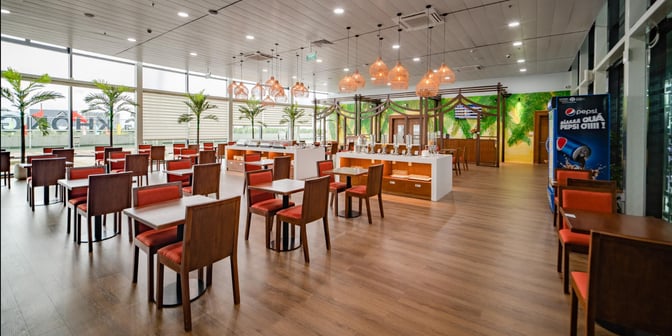The SH Premium Lounge at Phu Cat Airport features a spacious seating area with tables and chairs, adjacent to a self-serve food station.