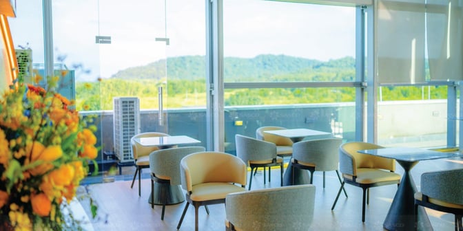 The seating area at SENS Leisure Lounge features tables and chairs with large windows offering views of the surrounding landscape.