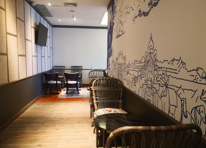 The seating area in Bangkok Airways Blue Ribbon Lounge at Phuket International Airport features wicker chairs and a mural wall design.