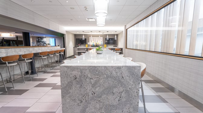 The Club PIT at Pittsburgh International Airport features a bar area with counter seating and a variety of displayed beverages.
