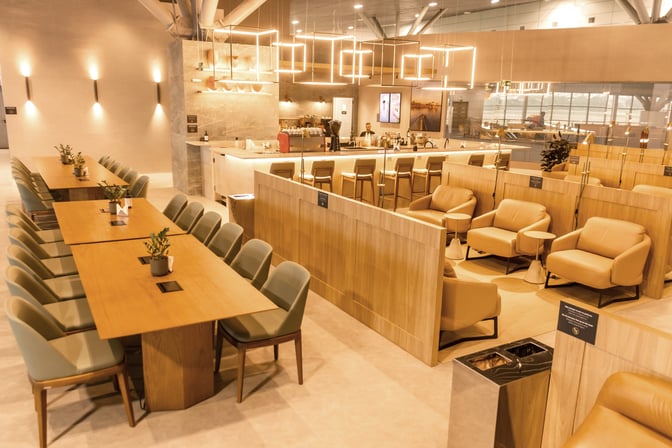 The W Premium Lounge at Porto Alegre Airport features a bar with counter seating and a spacious area with tables and chairs.