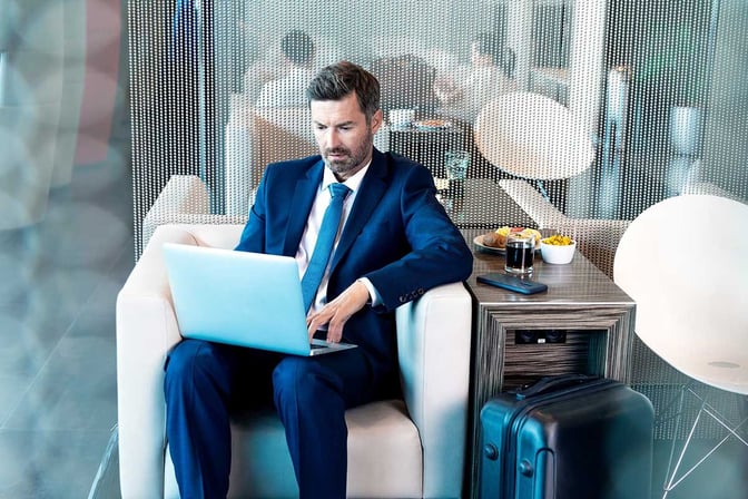 A man works on a laptop in a seating area at Erste Premier Lounge, with snacks and a drink on a side table.