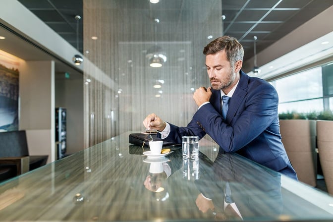 A man in a suit sits at a reflective counter in the Erste Premier Lounge, stirring a cup of coffee.