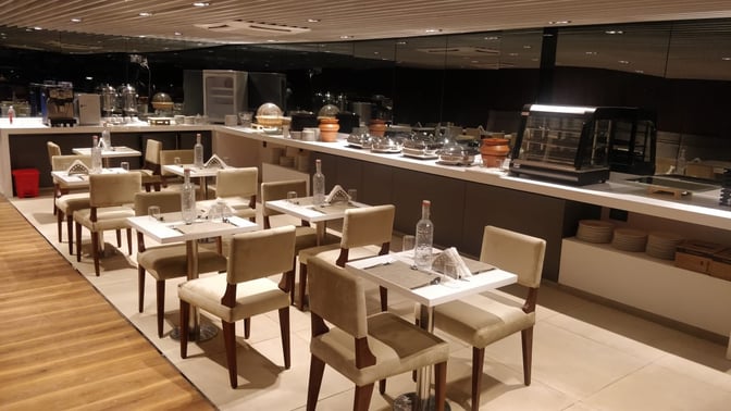 The dining area at Earth Lounge, Pune Airport, features table seating with a self-serve buffet counter offering various dishes.