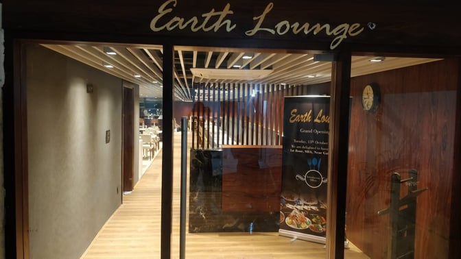 The entrance to Earth Lounge at Pune Airport features glass doors and a sign, leading to a seating area inside.