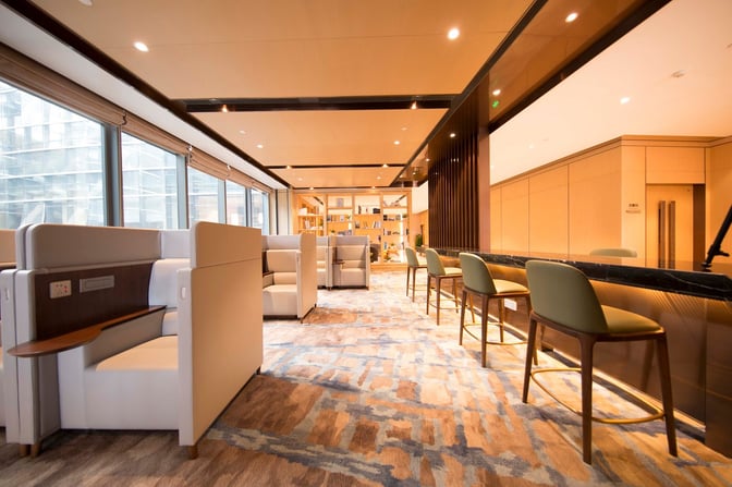 The Plaza Premium Lounge at Qingdao Liuting International Airport features booth seating with power outlets and a bar area with high chairs.