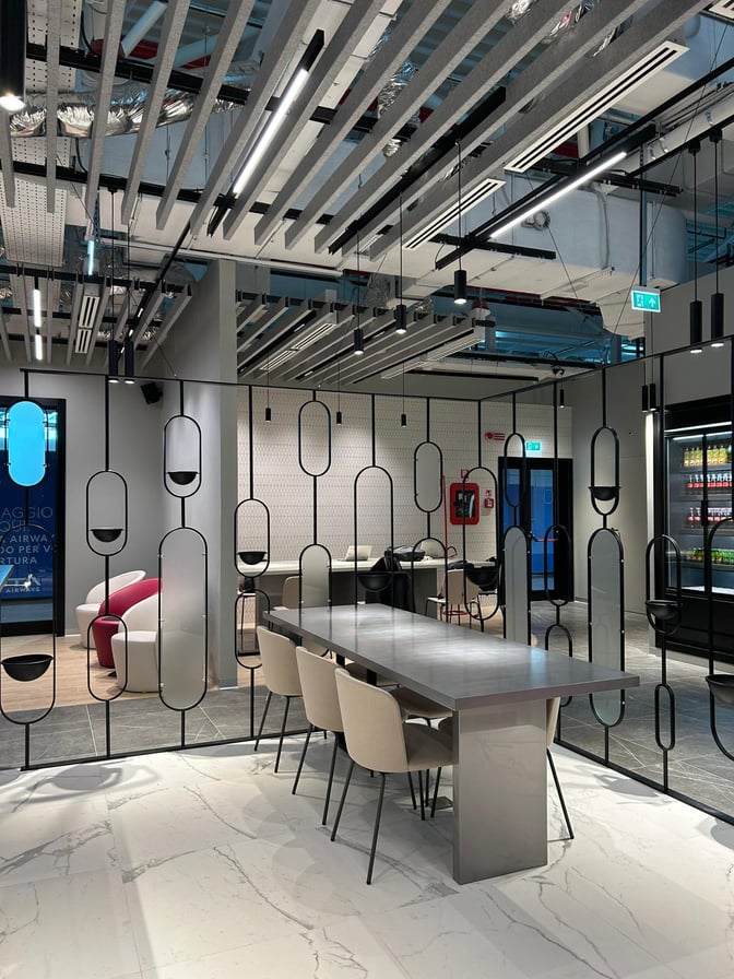 The Primeclass Lounge at Leonardo da Vinci-Fiumicino Airport features a communal table with seating and a partitioned area for privacy.