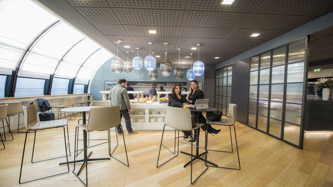 The Prima Vista Lounge at Leonardo da Vinci-Fiumicino Airport features a seating area with high tables and a self-serve food station.