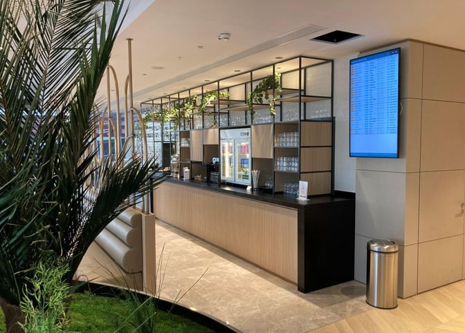 The Plaza Premium Marmara Lounge features a beverage counter with self-serve drinks and glassware, adjacent to a flight information screen.