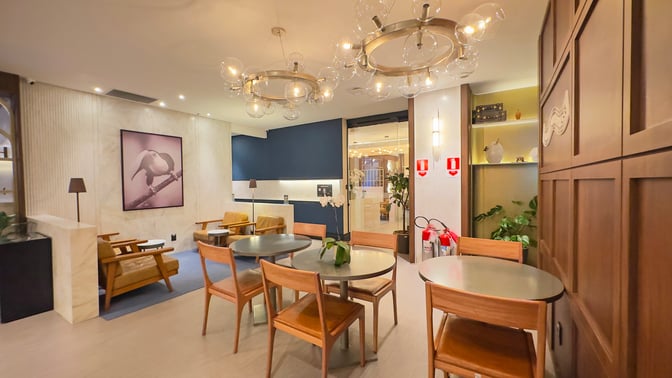 The seating area in the W Lounge Guarulhos features round tables and chairs, with artwork and fire safety equipment visible.