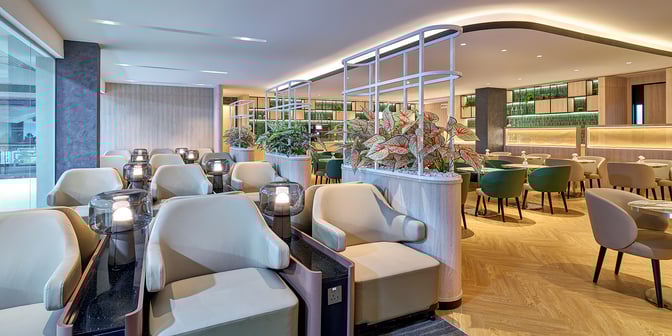 The seating area in Plaza Premium Lounge at Senai International Airport features comfortable chairs and tables, with decorative plants providing privacy.