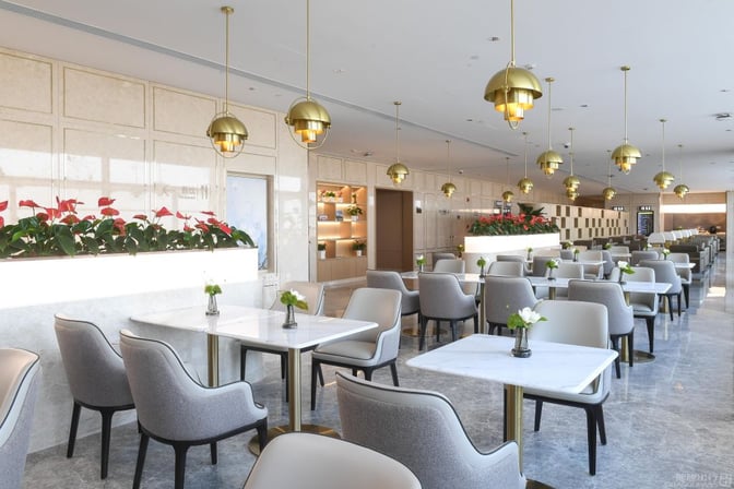 The seating area in No. 170 VIP Lounge at Shanghai Pudong Airport features tables with chairs and decorative plant arrangements.