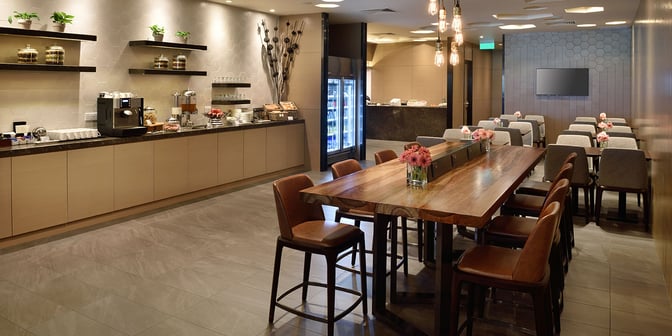 The Plaza Premium Lounge at Singapore Changi Airport features a self-serve beverage station and communal dining area with seating.