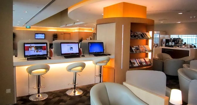 The SATS Premier Lounge at Singapore Changi Airport features a computer station with bar seating and a magazine rack nearby.