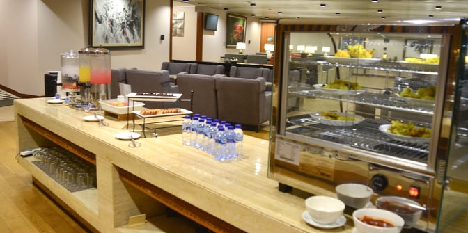 The Saphire Lounge at Soekarno-Hatta International Airport features a self-serve food and beverage station with seating in the background.
