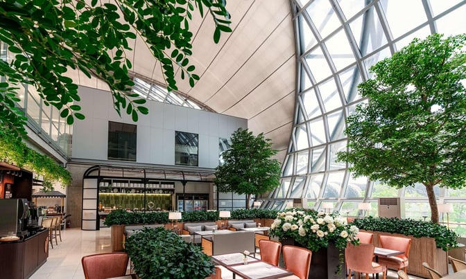 The Coral Executive Lounge at Suvarnabhumi Airport features seating areas with tables, surrounded by greenery and large windows.