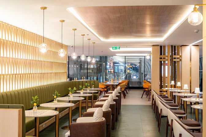 The Coral Finest Business Class Lounge at Suvarnabhumi Airport features a seating area with tables and chairs, offering airport views.