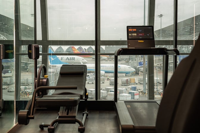 The Coral Finest Business Class Lounge at Suvarnabhumi Airport features a fitness area with exercise equipment overlooking the tarmac.