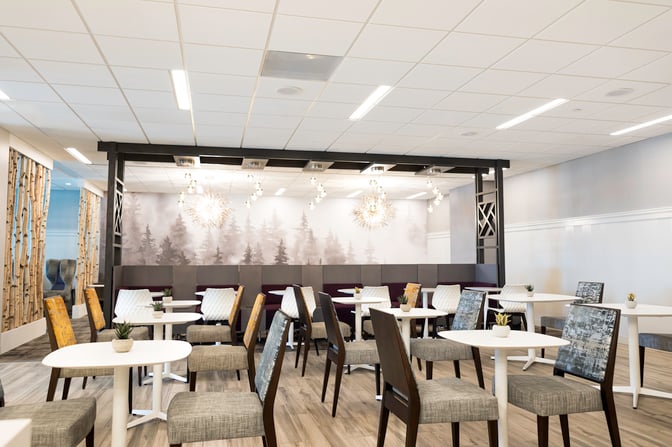The seating area in the Escape Lounge at Syracuse Hancock International Airport features tables and chairs with decorative wall art.