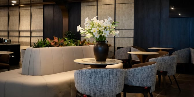 Seating area in the SENS Business Lounge at Tan Son Nhat International Airport features round tables, cushioned chairs, and decorative plants.
