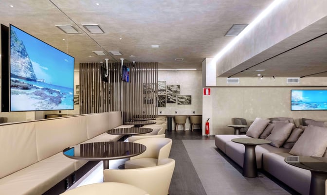 The BRT Lounge at Tancredo Neves International Airport features seating with tables and televisions for passenger relaxation.