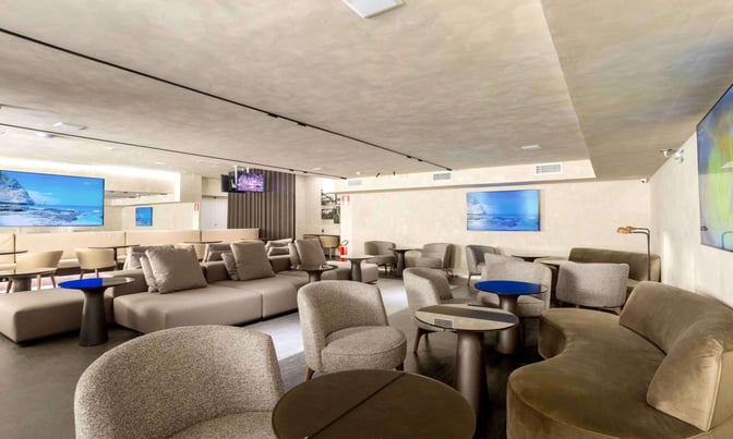 The BRT Lounge at Tancredo Neves International Airport features comfortable seating with tables and a large screen for entertainment.