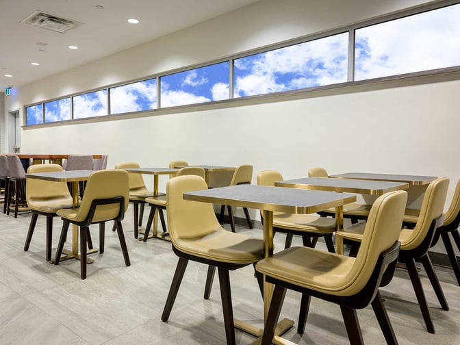 The seating area in Plaza Premium Lounge at Toronto Pearson Airport features tables and chairs with windows providing natural light.