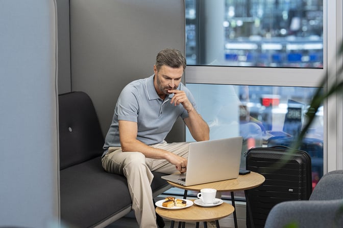 A traveler uses a laptop at a seating area in Prague's Fast Track Lounge, with a table holding snacks and coffee.