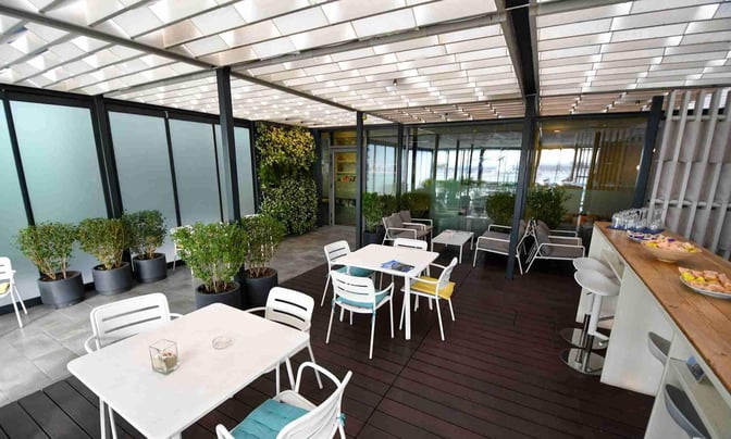 The outdoor seating area at Varna Airport's VIP Lounge features tables, chairs, potted plants, and a counter with snacks and drinks.