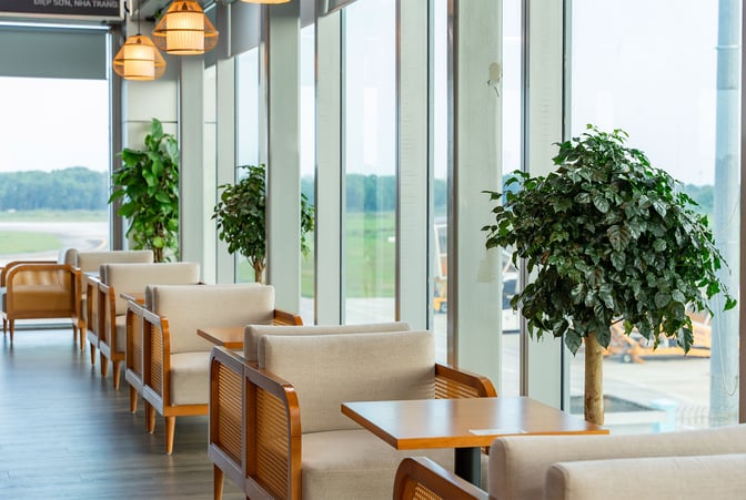 Seating area at SH Premium Lounge Vinh features cushioned chairs and tables with views of the airport runway through large windows.