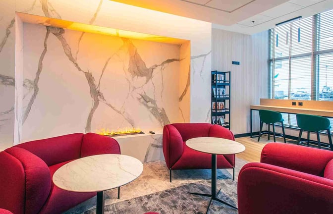 Seating area in the Etiuda Executive Lounge at Warsaw Chopin Airport features round tables, armchairs, and a view of the tarmac.