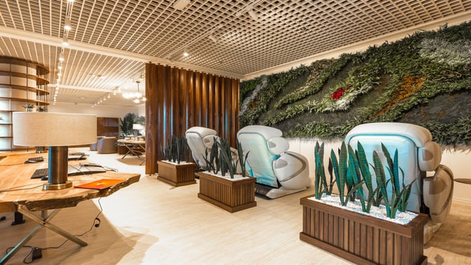 The Primeclass Lounge at Zagreb Airport features massage chairs and a work area with computers, set against a green wall installation.