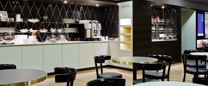 The Aspire Lounge at Zurich Airport features a self-serve beverage and snack area with tables and chairs for seating.