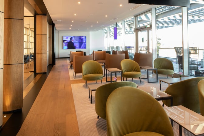 The Primeclass Lounge at Zurich Airport features a seating area with armchairs and tables, offering views through large windows.