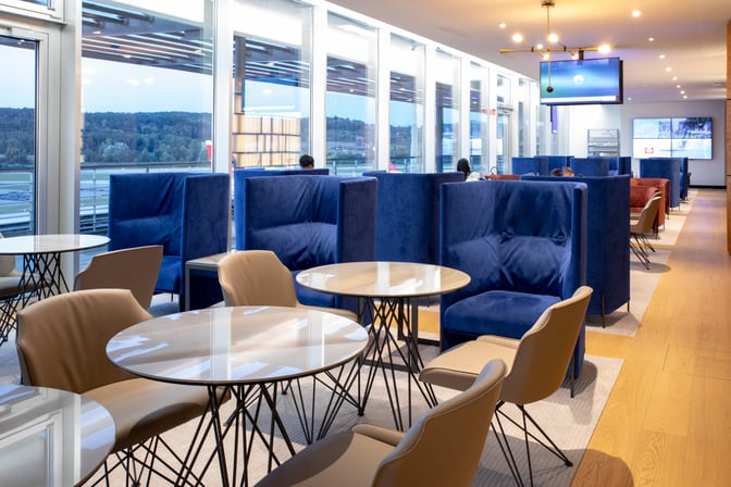 The Primeclass Lounge at Zurich Airport features semi-private booth seating with tables, offering views of the airport runway.