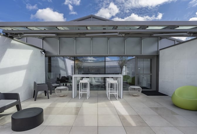 The outdoor seating area at A Coruña Airport's VIP Lounge features high tables, chairs, and casual seating options for relaxation.
