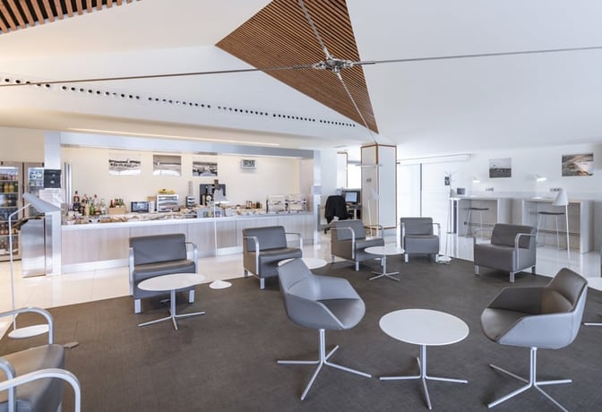 The VIP Lounge at A Coruña Airport features a seating area with chairs and tables, adjacent to a self-serve food and beverage counter.