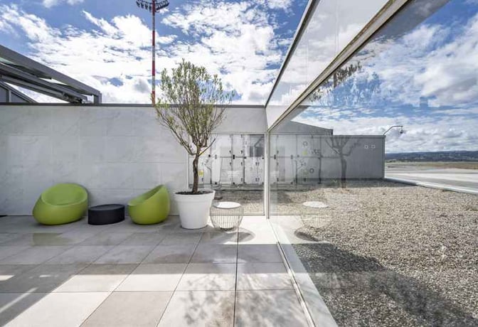 The outdoor seating area at A Coruña Airport's VIP Lounge features modern chairs and potted plants with views of the tarmac.