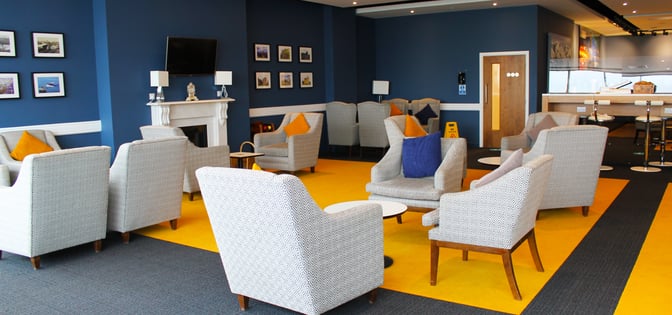 The Northern Lights Executive Lounge at Aberdeen International Airport features comfortable armchairs, a fireplace, and a wall-mounted TV for relaxation.
