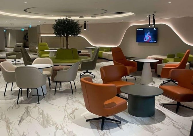 The seating area in the Pearl Lounge at Abu Dhabi International Airport features diverse chairs and tables with a television for entertainment.