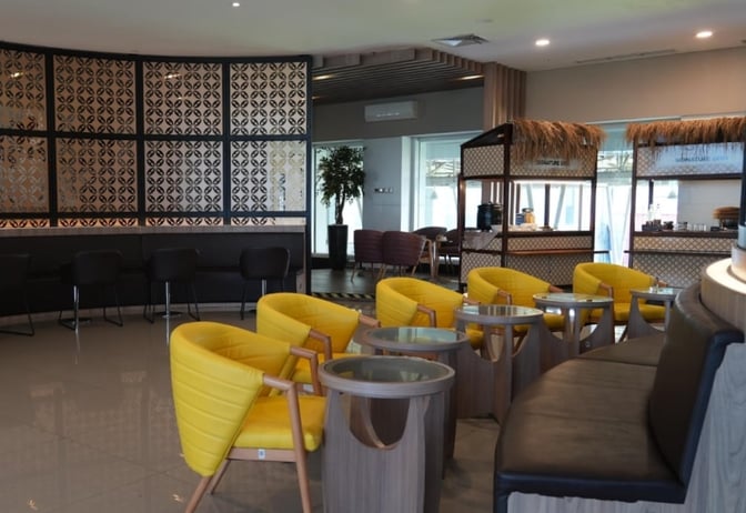 The Concordia Lounge at Achmad Yani International Airport features a seating area with tables and chairs, and a self-serve refreshment station.